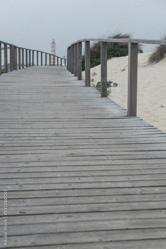Wooden walkways along the dunes of the beach of Barra with the Aveiro lighthouse in the background in a cloudy day. Portugal
