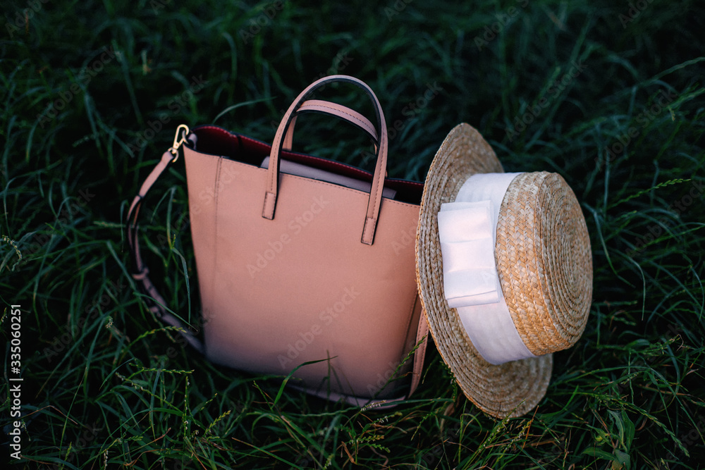 women handbag and boater with white ribbon on green grass. women handbag and boater with white ribbon on green grass.