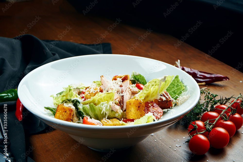 Caesar salad with croutons, parmesan, chicken, egg in black plate on colored background. Restaurant serving. Close up Caesar salad with croutons, parmesan, chicken, egg in black plate on colored background. Restaurant serving. Close up