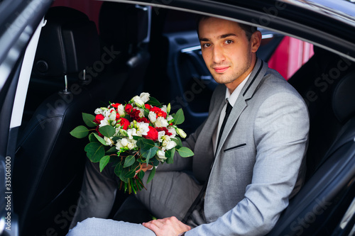 the groom sits in a car and holds a wedding bouquet