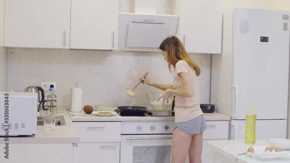 Sequence of shots of young attractive woman wearing home clothes standing at stove in the kitchen and making pancakes. Then she switching on cooker hood Sequence of shots of young attractive woman wearing home clothes standing at stove in the kitchen and making pancakes. Then she switching on cooker hood