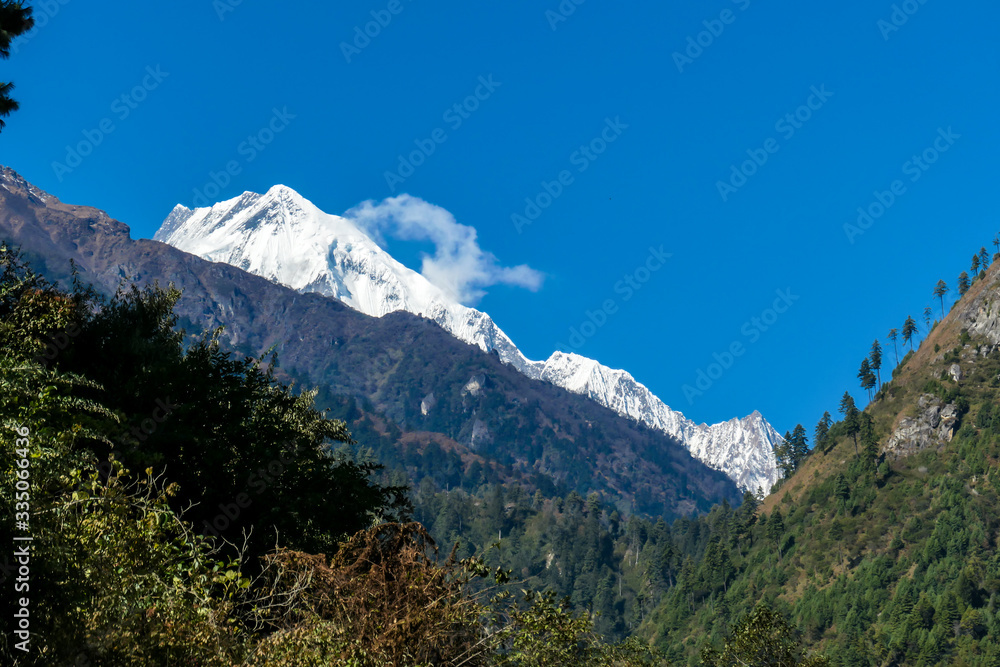 Fototapeta premium View on Himalayas, Annapurna Circuit Trek, Nepal. Early morning in the mountains. Lower parts of the mountains covered in shadow, high snow caped mountains peaks catching the first beams of sunlight