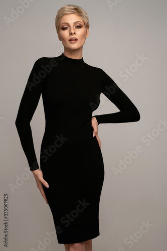 Sexy blonde woman wearing black classic dress posing over gray background