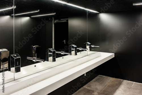 Foto Modern public restroom with black walls and row of white sinks