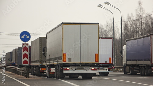 A many trucks rows queue next to quarantine control point at spring day rear side view, state isolation traffic, illustration concept 