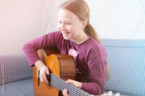 happy active girl playing guitar. ginger haired teenager smiling and learning to play music on acoustic gutar. indoors activity. stay at home concept. photo