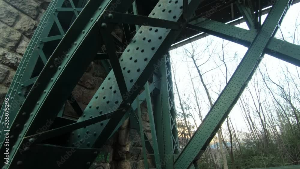 Pan down underneath view of a green bolted railroad steel bridge ...
