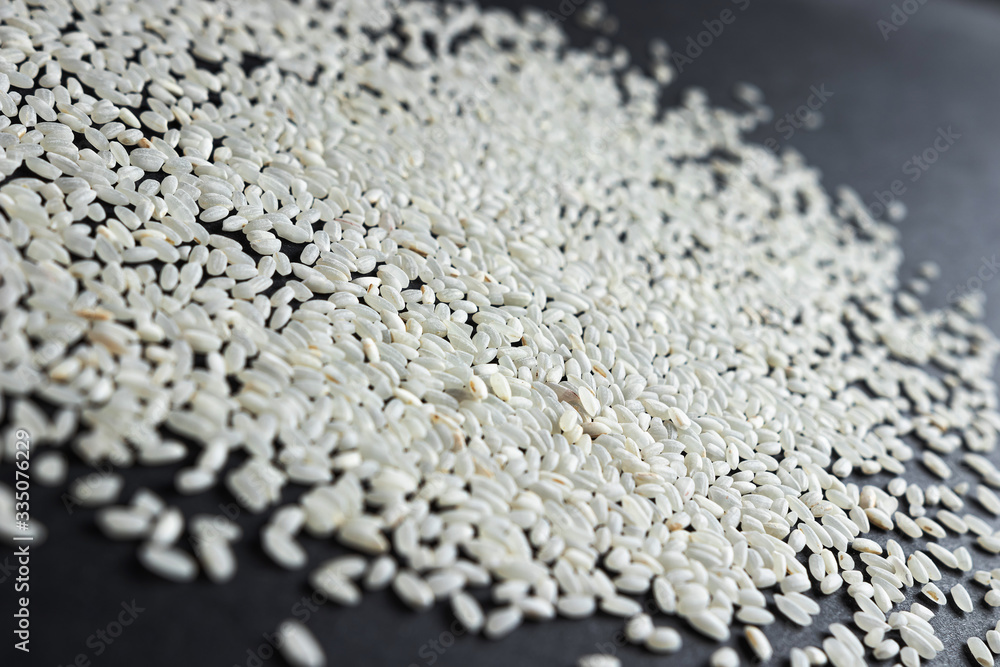 a lot of white long grain rice for pilaf or porridge on black paper