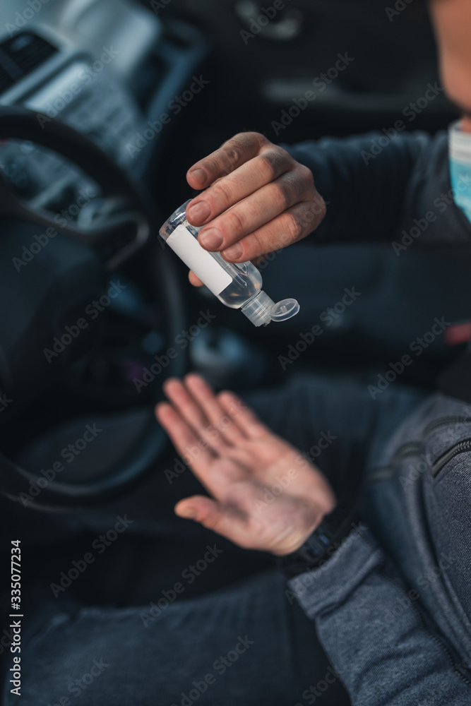 A man use an antiseptic gel into his hands while sitting in a car. A man in a medical mask to protect viruses. masked man in a car. coronavirus, disease, infection, quarantine, covid-19