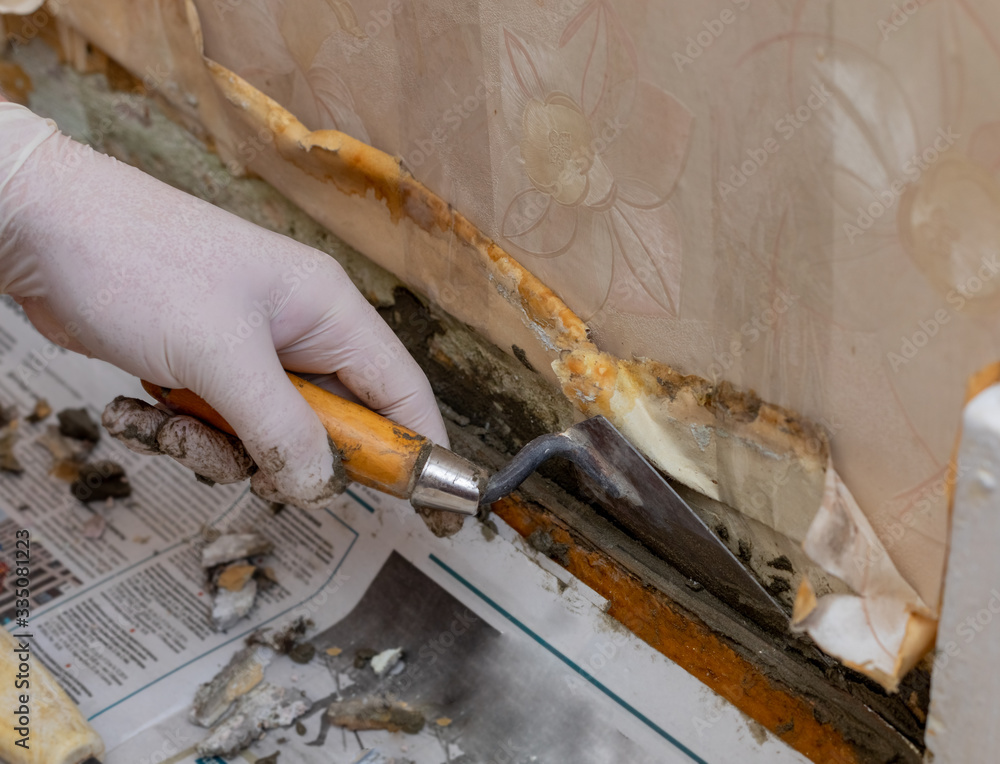 A gloved hand is spreading cement on a wall with a trowel. Construction