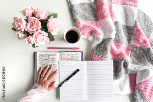 Devotional Bible study. Woman's hand is turning a page of the Bible. With pink roses, black tea and coffee. Background pink, white and grey colors. Baselland, Switzerland - 02.04.2020