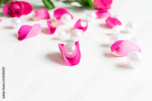 Pink, white, green flat lay: Pearls, pink rose petals, on white bright background. Beautiful set up. Top view, copy space, mock up. 