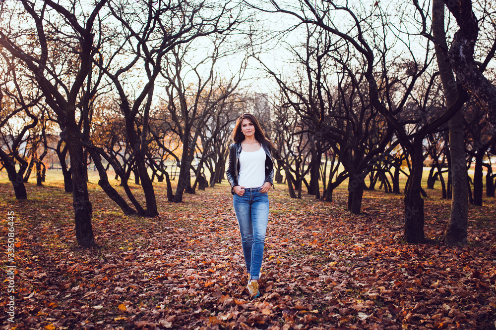 A happy brunette in jeans and a leather jacket in an apple orchard on a walk is an energetic young successful woman A happy brunette in jeans and a leather jacket in an apple orchard on a walk is an energetic young successful woman