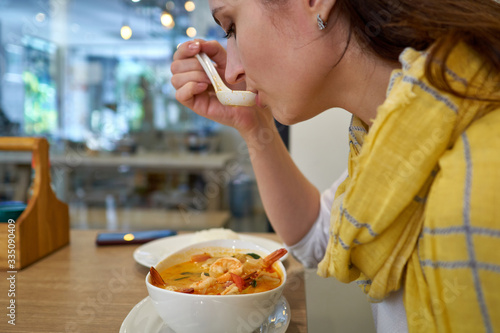 Woman eating Tom Yum Kun soup with shrimps in Thai restaurant, Bangkok, Thailand.