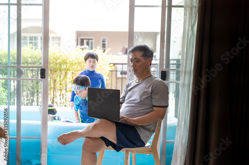 A grandfather is working while he watches his sons swim in a small pool in house.