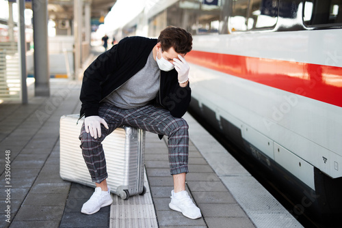 Ein Mann verzweifelt auf einem Bahnsteig, wegen dem Coronavirus trägt er eine Atemmaske und Gummihandschuhe