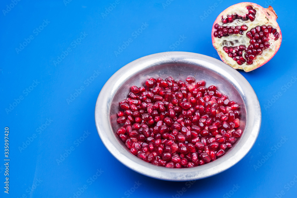 Pomegranate grains in a metal plate and half ripe pomegranate on a blue background Pomegranate grains in a metal plate and half ripe pomegranate on a blue background
