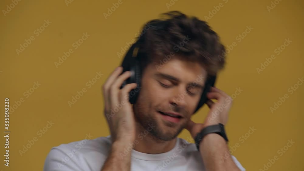 Man with closed eyes dancing in headphones isolated on yellow Man with closed eyes dancing in headphones isolated on yellow