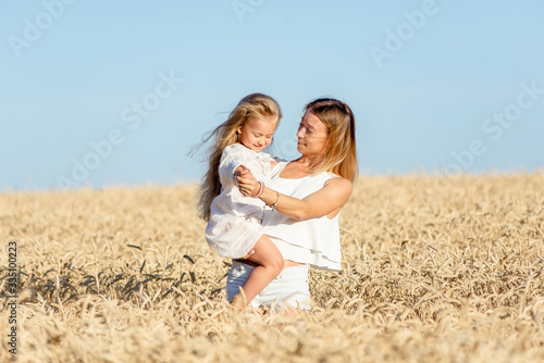 A young woman stands in a wheat field in the summer and holds her little daughter in her arms.