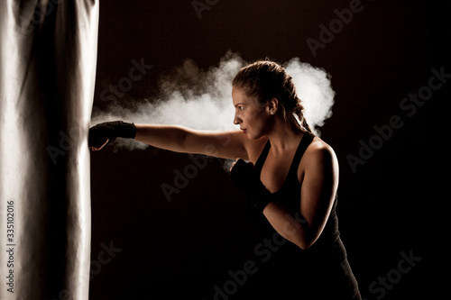 kick fighter girl punching a boxing bag. smoke and dark background