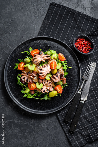 Salad with grilled octopus, potatoes, arugula, tomatoes and olives. Black background. Top view