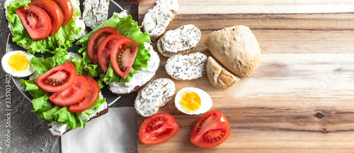 Sandwiches and eggs for healthy snack/lunch. Hard boiled eggs and sandwiches with cream cheese, tomatoes, lettuce and rye bread on the wooden board. Sandwiches with cheese. Layout decision.