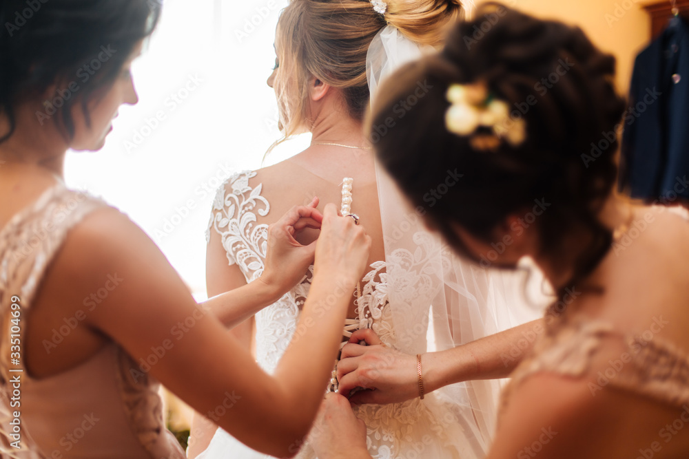 bride's girlfriend prepares the bride for her wedding day. The bride's girlfriend helps secure the bride's wedding dress before the ceremony bride's girlfriend prepares the bride for her wedding day. The bride's girlfriend helps secure the bride's wedding dress before the ceremony