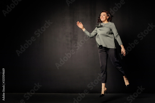 Successful business woman in a gray blouse jumps and rejoices on black background. Free space. Attractive businesswoman on a black background. Copy space