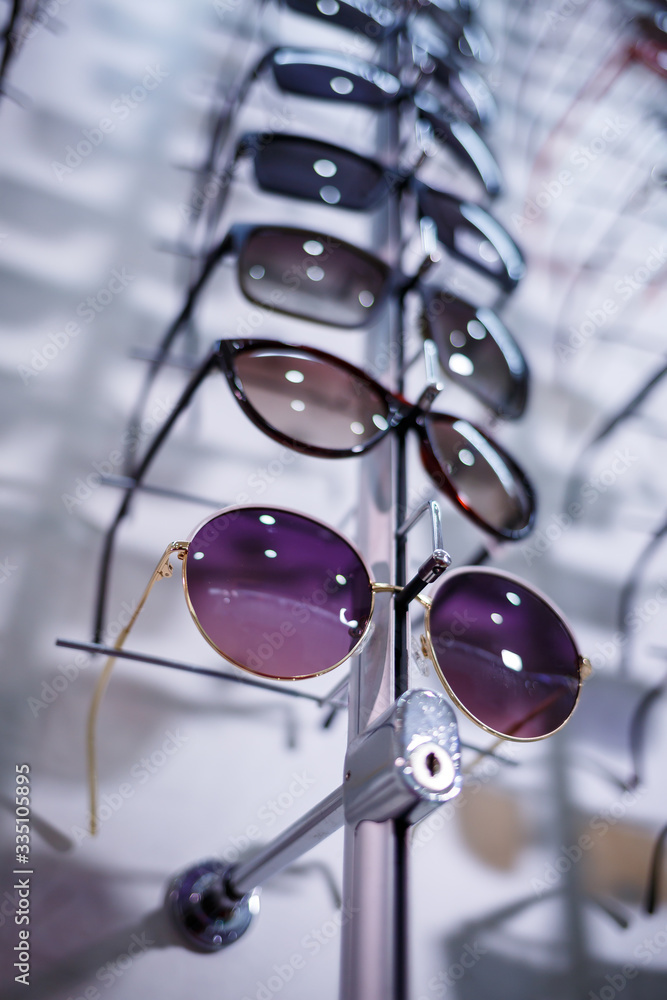 A row of glasses to protect from the sun. Store points. Stand with sunglasses in the optics store. Female hand shows glasses. Presentation of points. Close-up A row of glasses to protect from the sun. Store points. Stand with sunglasses in the optics store. Female hand shows glasses. Presentation of points. Close-up