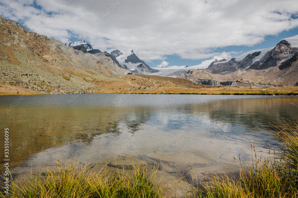 Small red tourists shelter house and mountains lake with snowy peaks of Swiss Alps reflection