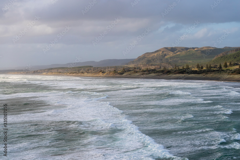 aerial landscape of sunset over Muriwai beach with waves in the foreground and a typical New Zealand coastal landscape