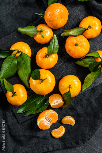 Fresh mandarin oranges fruit or tangerines with leaves in a wooden bowl. Gray background. Top view