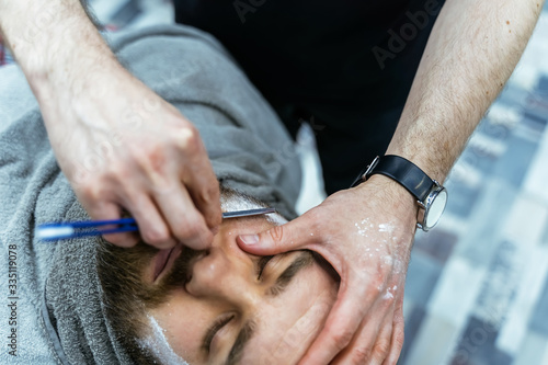 Shaving process of beards in Barbershop. Close up shot of barber makes a haircut beard client with straight razor.