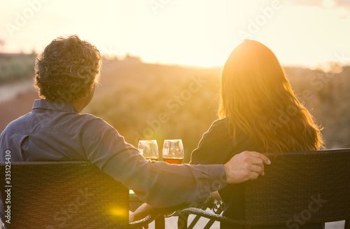 Man and Woman Sitting with Wine Glasses Overlooking Vinyard at Sunset photo