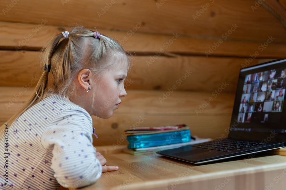 Cute adorable caucasian little blond girl siiting at desk with laptop during online video chat scholl lesson session with teacher and class. Remote education concept. Self-isloation at quarantine Cute adorable caucasian little blond girl siiting at desk with laptop during online video chat scholl lesson session with teacher and class. Remote education concept. Self-isloation at quarantine