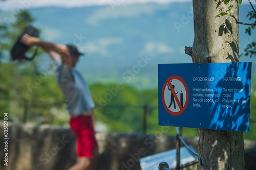 Man throwing an object over a fence despite the warning sign or board prohibiting throwing rocks. Reckless or ignorant behavior of visitors in nature.
