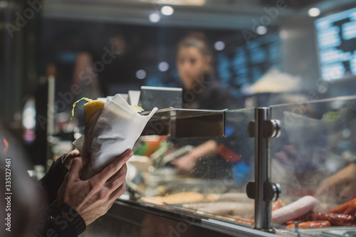 Photography Person holding a fresh kebab or gyros in his hands in front of a fast food vendor or stall