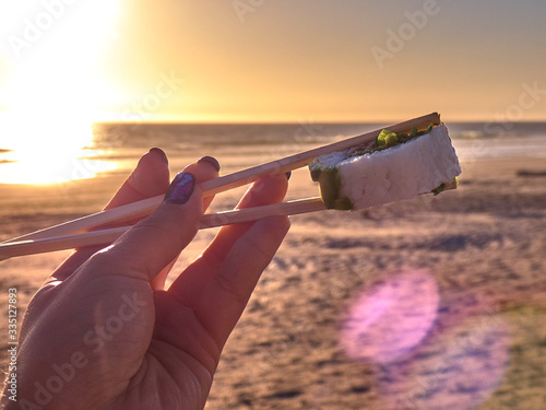 Woman holding sushi at sunset on the beach photo