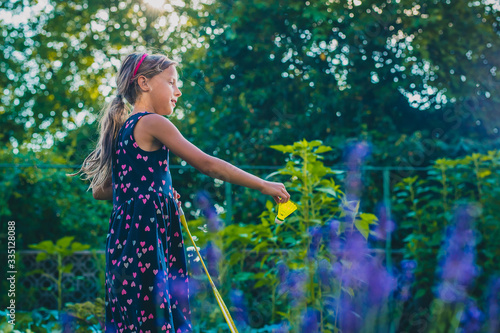 Young caucasian girl or kid is playing badminton game in a lush green garden. Kid holding shuttlecock and is preparing to serve.