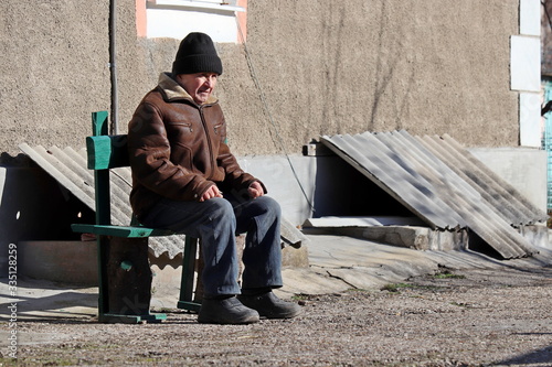 Foto Elderly man sitting on wooden bench in the yard of his home during the quarantine of covid-19 coronavirus pandemic