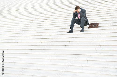 Tableau sur toile Depressed businessman sitting outdoors on a large white staircase hanging his he