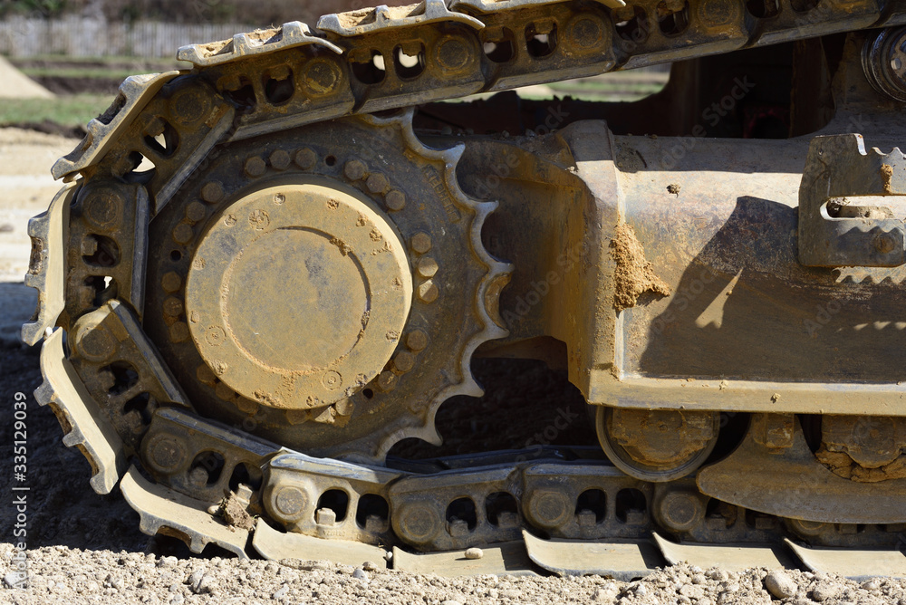 Detail and close-up of the metal wheels and the wheel chain of an excavator on a construction site with soil and dirt