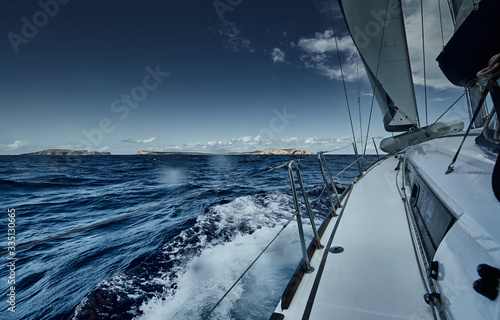 The view of the sea and mountains from the sailboat  edge of a board of the boat  slings and ropes  splashes from under the boat  sunny weather  dramatic sky