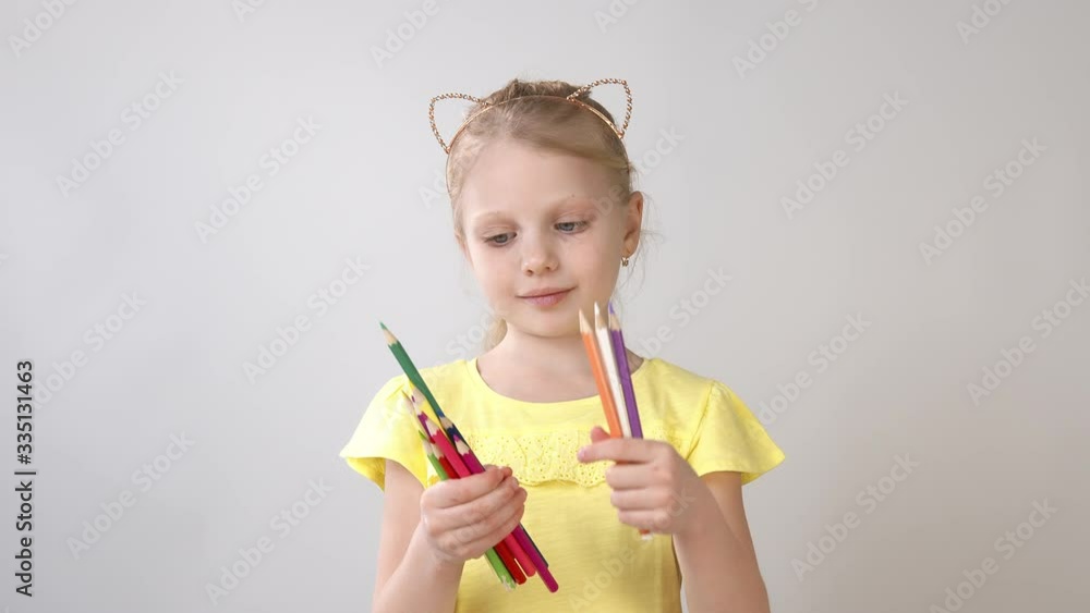 A little girl holds colored pencils in her hands. The girl is preparing to draw. A little girl holds colored pencils in her hands. The girl is preparing to draw.