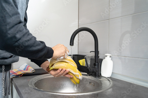 Side view on hands of unknown caucasian man person holding bananas under the sink tap washing fruit with soap cleaning disinfection in water to disinfect from viruses or pollution at home in kitchen