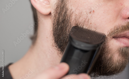 A man shaves his beard with a trimmer