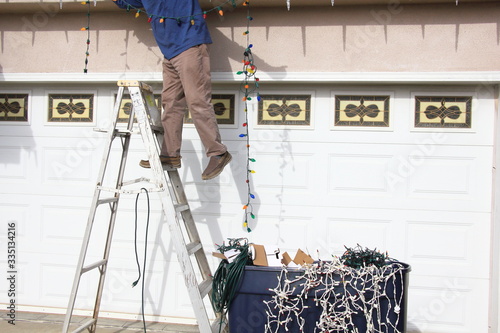 Man stringing Christmas lights on his house.