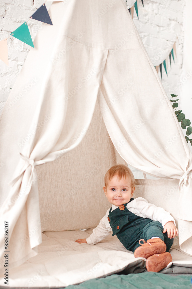 The little boy is playing near the wigwam. The little boy is playing near the wigwam.