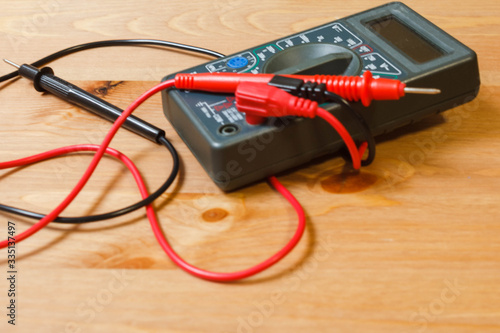 Multimeter for measuring current and voltage. Multimeter with electrodes and wires for measuring and testing volts and amps in various power sources on a wooden background