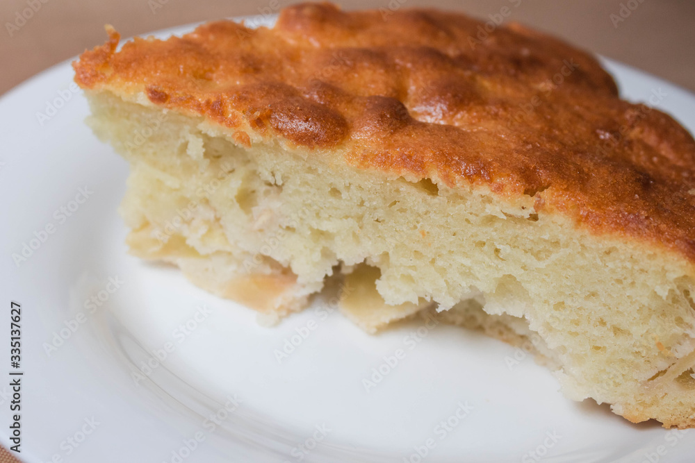 Sweet homemade cakes with apples. A slice of sponge Apple pie with a ruddy crust on a white plate close-up on a beige textile linen background. Sweet homemade cakes with apples. A slice of sponge Apple pie with a ruddy crust on a white plate close-up on a beige textile linen background.